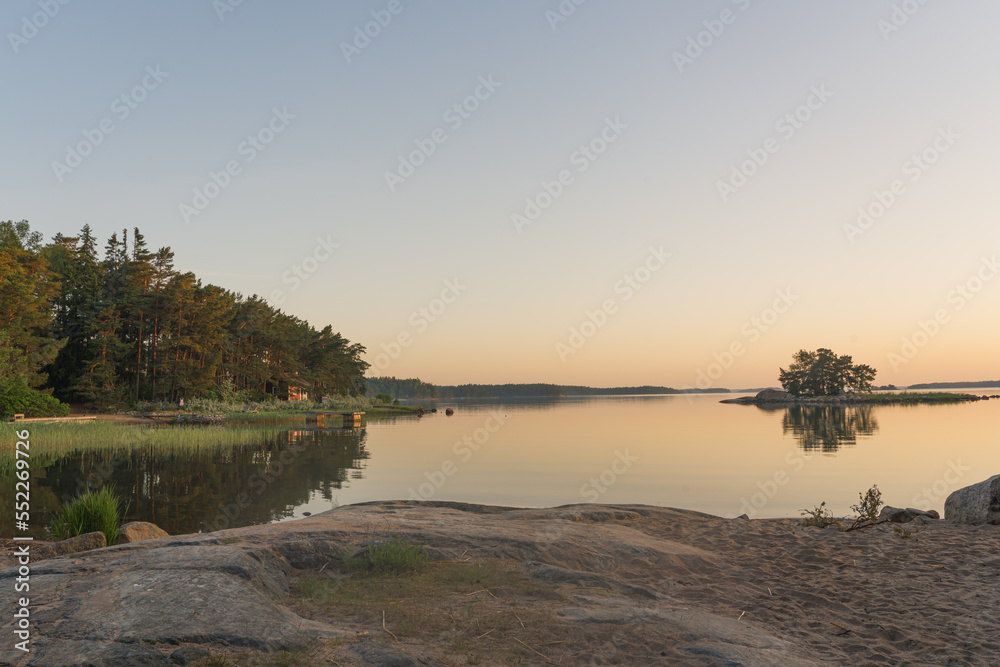 Nagu, Finland - 12.06.2022: Quiet sea shore after sunset. A line of trees and a small island on the horizon. Rocky coast in the foreground. Nature of Finland. Natural background. Space for text. Nagu, Finland - 12.06.2022: Quiet sea shore after sunset. A line of trees and a small island on the horizon. Rocky coast in the foreground. Nature of Finland. Natural background. Space for text.