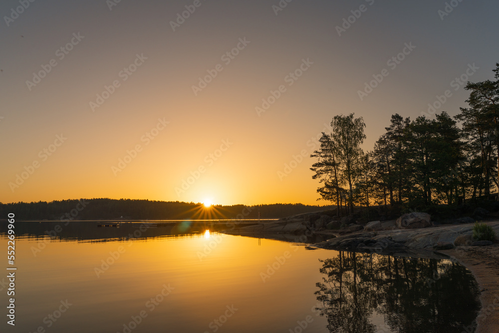 Fototapeta premium A golden-orange sunset on the sea with a silhouette of a tree line on the horizon. Nature of Finland. Scandinavia. Natural background. Space for text.
