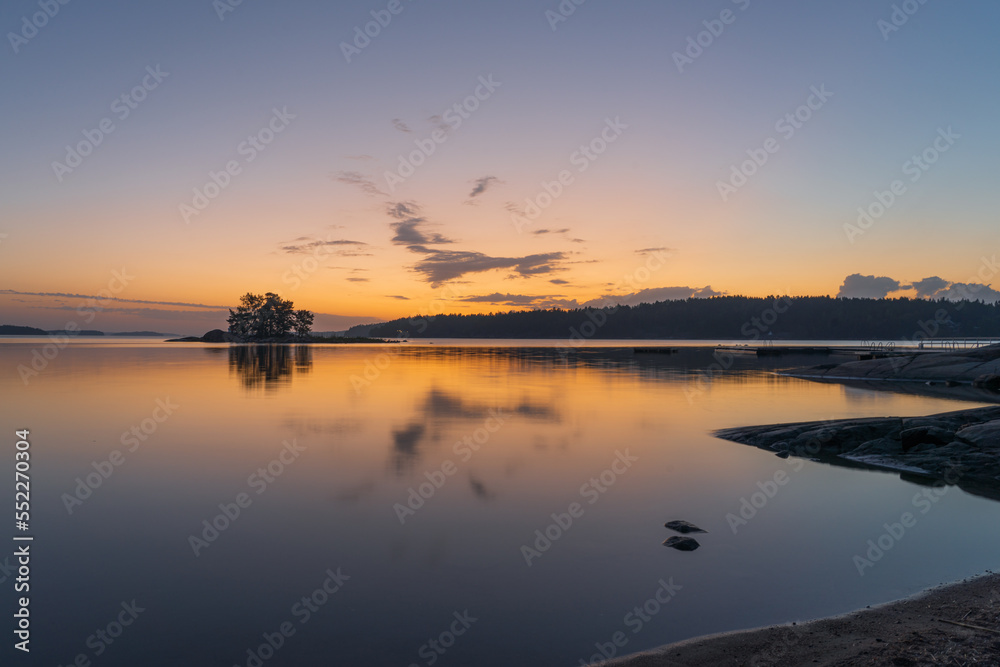 An orange-blue sunset on the sea with a silhouette of a tree line on the horizon. Nature of Finland. Scandinavia. Natural background. Space for text.