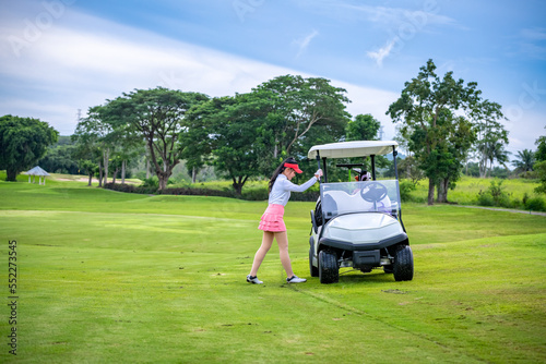 Professional woman stand near Golf cart and golf club putting on green grass at course with sun sky background 