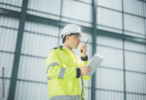 warehouse manager with tablet and ..radio communication his worker working in background in warehouse distribution center environment. Business warehouse inventory,contruction warehouse