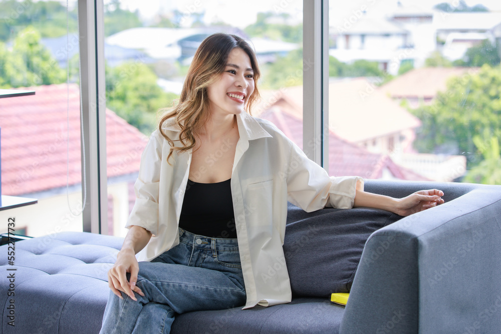 Obraz premium Millennial Asian young beautiful professional female dressmaker designer sitting on cozy sofa at tailor workshop studio.