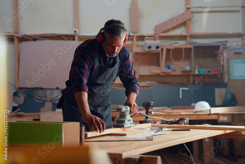 Mid adult man working with power tools and timber on table in woodworking factory
