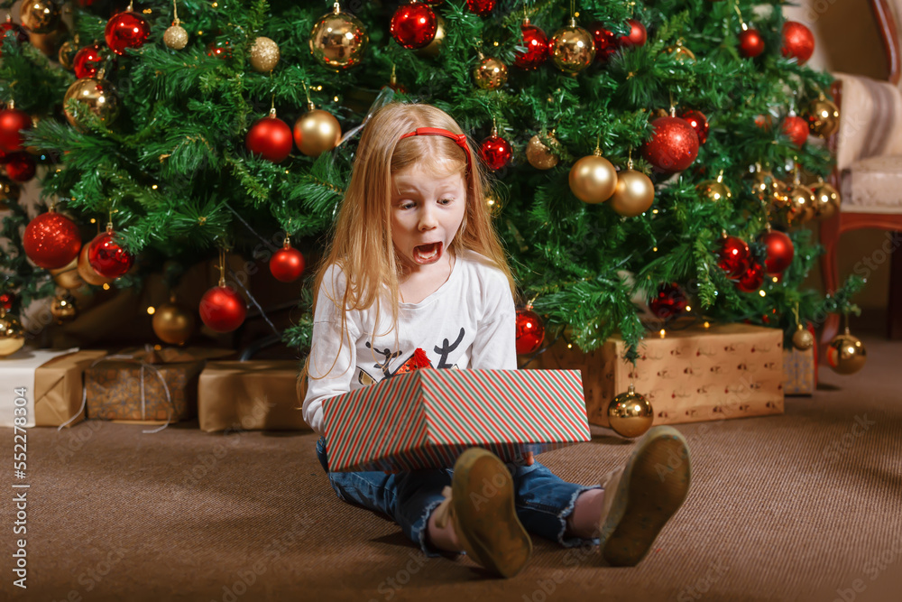 A bright emotions of a child for a Christmas gift sitting next to the Christmas tree A bright emotions of a child for a Christmas gift sitting next to the Christmas tree