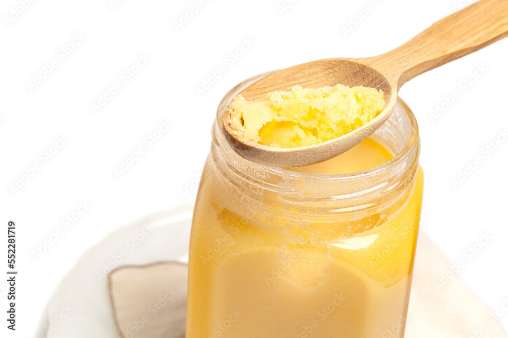 Ghee in jar and wooden spoon isolated on white background