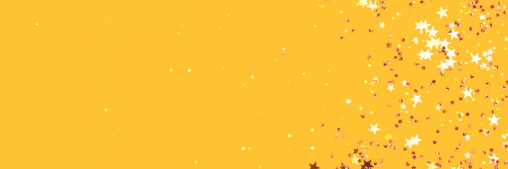 Golden stars and crystals confetti scattered on a yellow background. Festive concept with copy space. Selective focus.