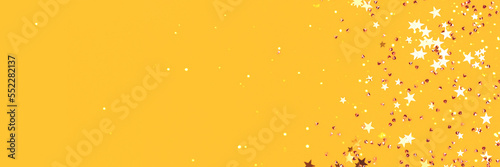Golden stars and crystals confetti scattered on a yellow background. Festive concept with copy space. Selective focus.