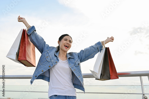 Carefree and overjoyed Asian female carrying her shopping bags, happy with Black Friday sales.