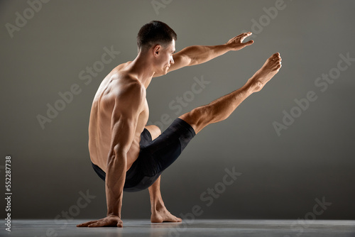 Portrait of male flexible muscular athlete showing animal flow sport elements isolated over gray background. Fitness, trendy sports, beauty of body