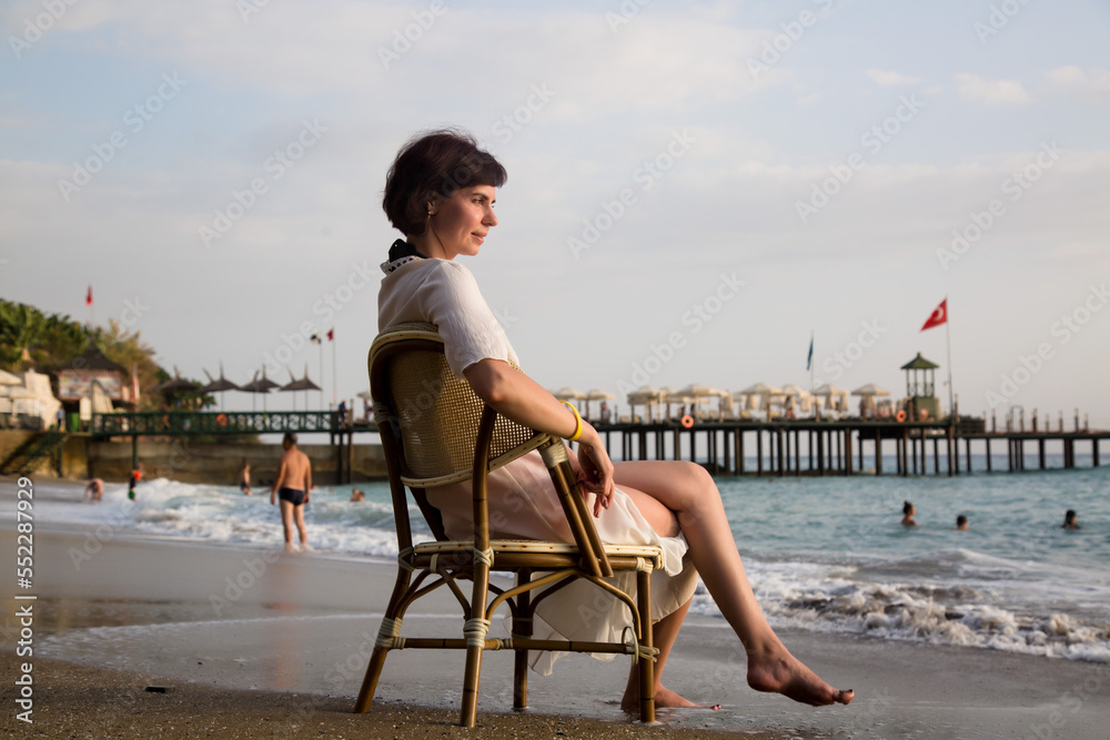 Happy woman sitting on a chair near the sea waves and enjoying the sea view.