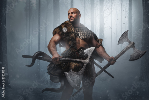 Studio shot of bald viking warrior with fur holding two huge axes in frost wood.