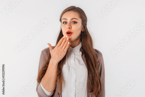 Amazed young woman showing Oops expression at the camera. Portrait of young girl with long hair, arm cover mouth, standing against white studio background