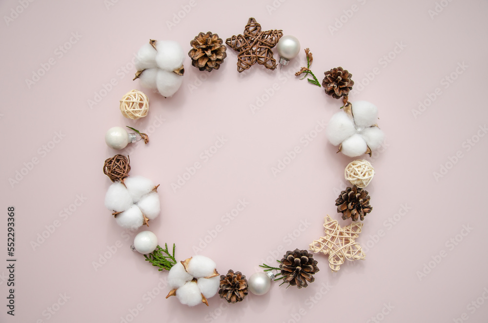 Christmas winter round frame of thuja branches, cotton flowers, fir cones, straw stars and balls on rose background. Flat lay, top view, copy space Christmas winter round frame of thuja branches, cotton flowers, fir cones, straw stars and balls on rose background. Flat lay, top view, copy space