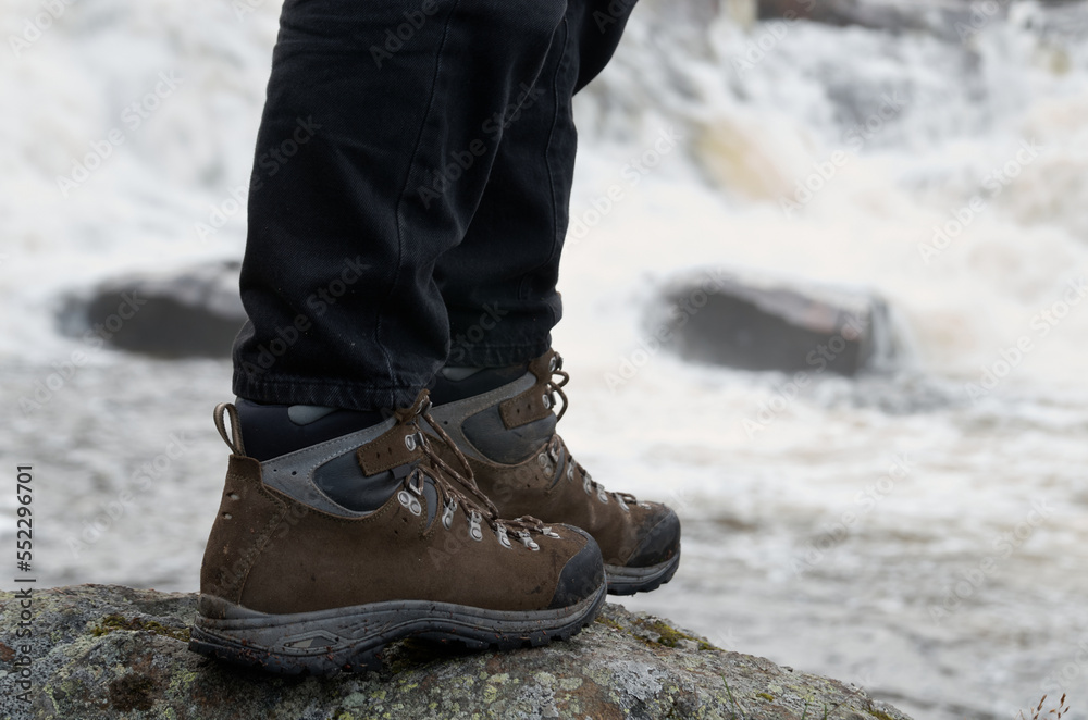 Close-up of legs in tourist boots standing on a stone against a background of a waterfall Close-up of legs in tourist boots standing on a stone against a background of a waterfall