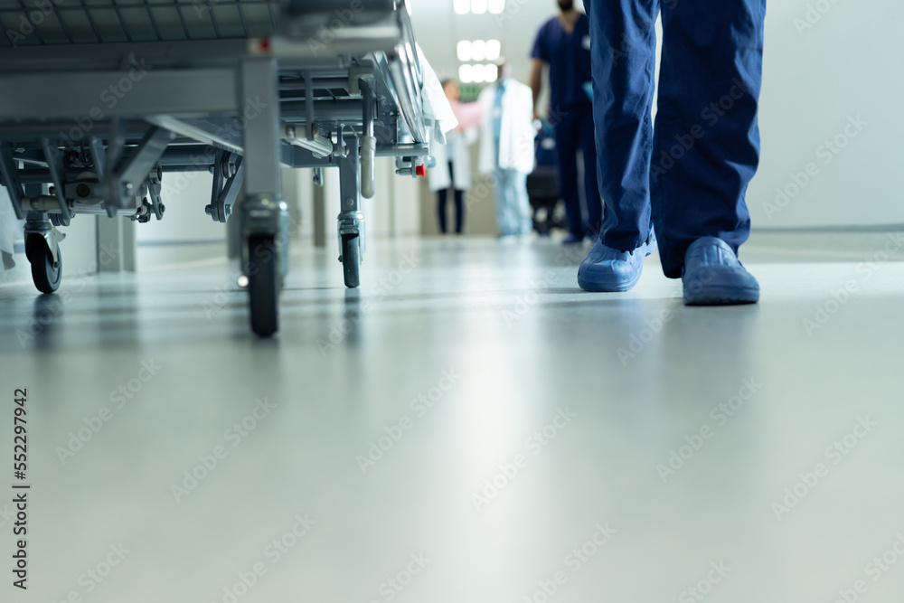 Low section of legs of hospital workers walking and hospital bed in corridor, with copy space
