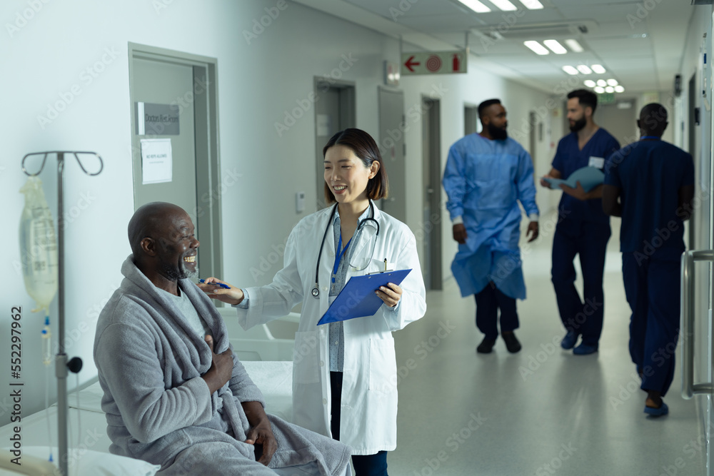 Asian female doctor and senior african american male patient smiling together in hospital corridor Asian female doctor and senior african american male patient smiling together in hospital corridor