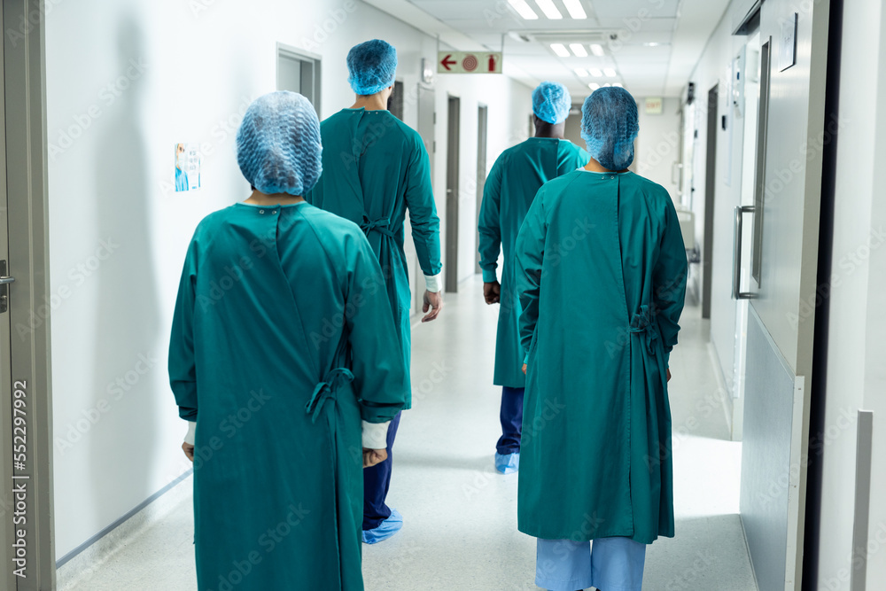 Rear view of four surgeons in surgical caps and gowns walking in hospital corridor Rear view of four surgeons in surgical caps and gowns walking in hospital corridor