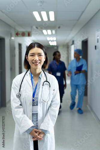 Vertical portrait of smiling asian female doctor in hospital corridor, copy space
