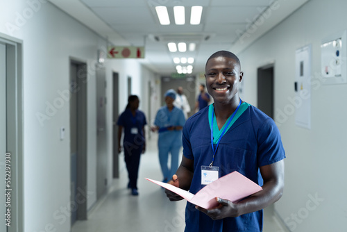 Portrait of smiling african american male healthcare worker in busy hospital corridor, copy space