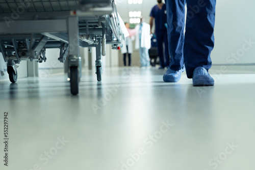 Low section of legs of hospital workers walking and hospital bed in corridor  with copy space