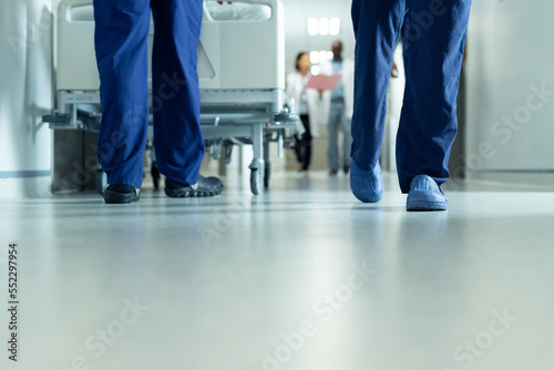 Low section of legs of hospital workers walking and hospital bed in corridor, with copy space