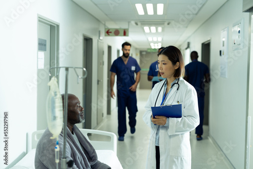 Asian female doctor and senior african american male patient talking in hospital corridor