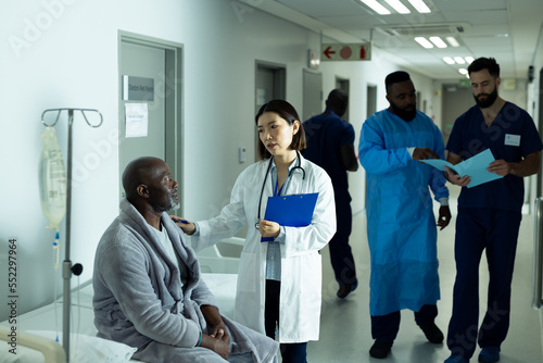 Asian female doctor consoling senior african american male patient in hospital corridor