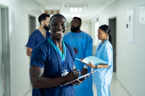 Portrait of smiling african american male healthcare worker writing in busy hospital corridor