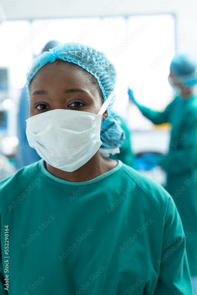Vertical portrait of african american female surgeon wearing face mask in operating theatre