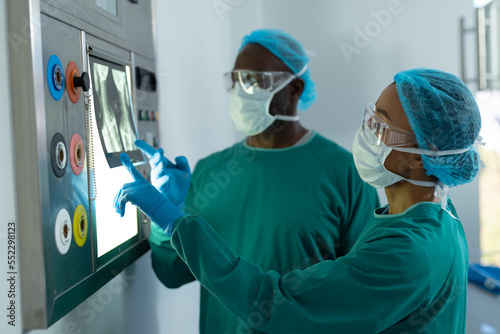 Two diverse surgeons studying x-ray on lightbox in operating theatre