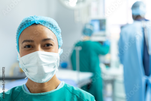 Portrait of smiling biracial female surgeon in mask in operating theatre  with copy space
