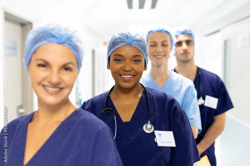 Portrait of diverse group of healthcare workers wearing surgical caps smiling in hospital corridor