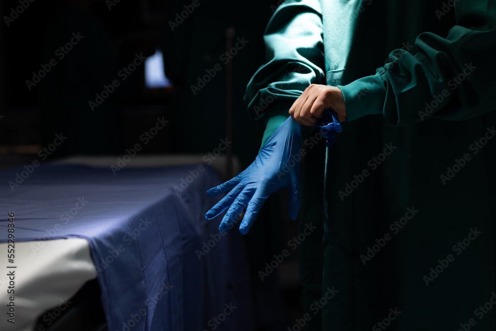 Midsection of surgeon putting on glove in dark operating theatre, with copy space