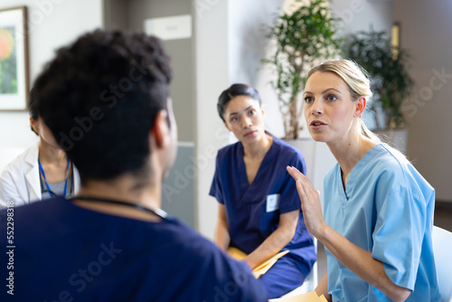Caucasian female doctor sitting talking with diverse colleagues at hospital