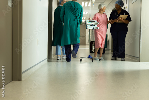 Diverse female doctor and caucasian senior female patient with iv pole talking in hospital