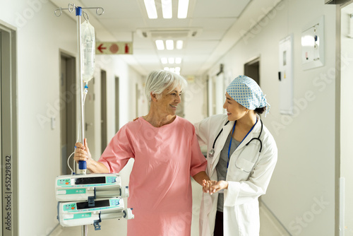 Diverse female doctor and caucasian senior female patient with iv pole talking