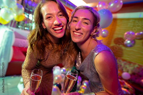 Portrait of two happy caucasian female friends laughing and drinking champagne at a nightclub