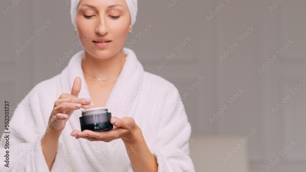 Young attractive woman in a bathrobe applies cream on her face in the bathroom. Young attractive woman in a bathrobe applies cream on her face in the bathroom.