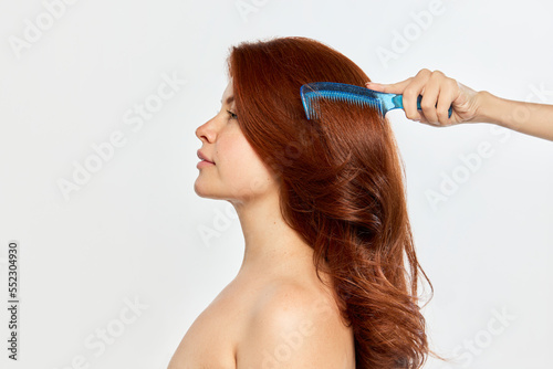 Portrait of young beautiful woman, with perfect red-haired woman taking care after hair with brushing isolated on white background