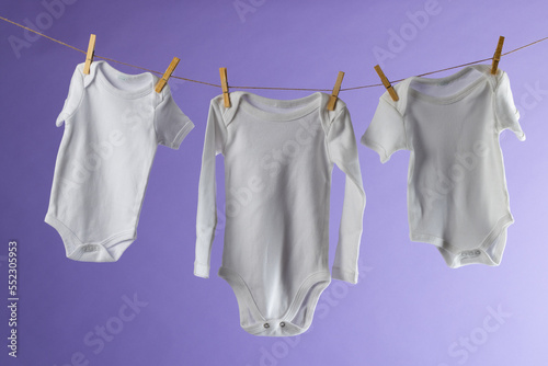 Baby clothes hanging on string and copy space on purple background