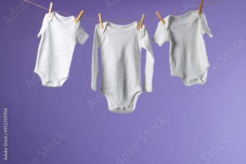 Baby clothes hanging on string and copy space on purple background