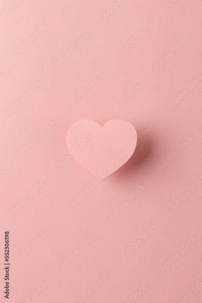 Vertical of elevated pink heart shape and shadow on pink background with copy space