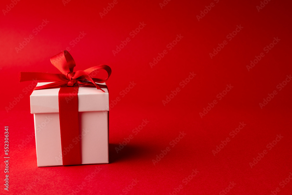 White gift box tied with red ribbon, on red background with copy space White gift box tied with red ribbon, on red background with copy space