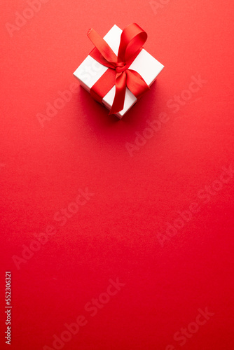 Vertical overhead of white gift box tied with red ribbon, on red background with copy space