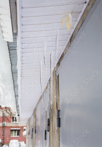 Icy, frozen icicles hang through cracks, spring or winter. Modern plastic cornice. Large cascades of icicles hang in disarray. Cloudy winter day, soft light.