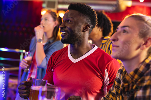 Diverse group of excited male and female friends watching sports game showing at a bar photo