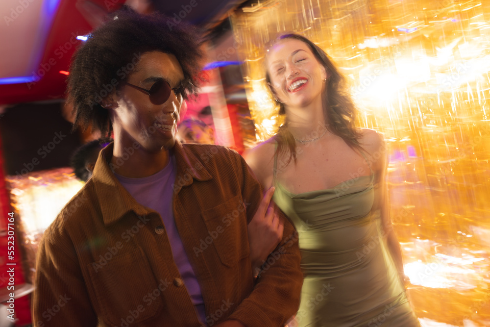 Happy, diverse couple laughing and walking arm in arm into a nightclub Happy, diverse couple laughing and walking arm in arm into a nightclub