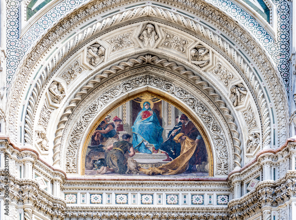 Close up on the façade of the Santa Maria del Fiore church or Florence Cathedral in neo-gothic style with white, green and red marbles, bas reliefs and frescoed lunette. 