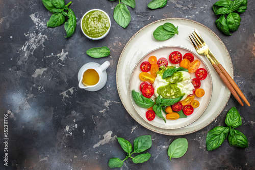 Salad with burrata cheese, cherry tomatoes and green pesto on a dark background. Restaurant menu, dieting, cookbook recipe top view