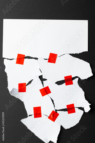 Ripped up pieces of white paper stuck together with red tape with copy space on black background